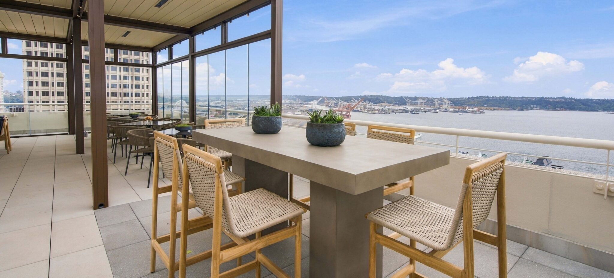 The Penthouse outdoor lounge by day: a high table and woven bar stools beside a covered pergola, overlooking Puget Sound